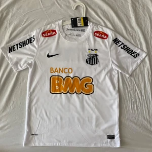 Vit Santos Neymar Jr fotbollströja Nike - Santos FC Neymar Jr matchtröja från Nike i vitt med svarta och gula detaljer. Kortärmad modell i Dri-FIT material som andas. Tryck med sponsorloggor, klubbmärke, nummer 11 och Neymar Jr på ryggen. Perfekt för dig som älskar brasiliansk fotboll.