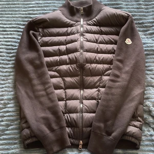 Svart Moncler cardigan - Snygg svart cardigan från Moncler med quiltad framsida och ärmar i mjuk bomull. Jackan har hög krage, hel dragkedja och Moncler-logga på ärmen. Perfekt för dig som vill ha en stilren och look med premiumkänsla. Äkta) hör av er vid fler frågor 