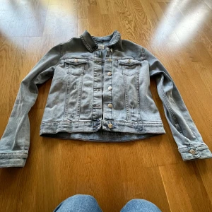 Ljusblå jeansjacka från KappAhl - Snygg ljusblå jeansjacka från KappAhl i klassisk modell med knappar framtill och två bröstfickor. Jackan har långa ärmar. Perfekt att slänga över en hoodie eller t-shirt. Den har några märken på ryggen där som syns på bild 4 men jag har aldrig använt den så troligtvis är den gjord så men jag är inte helt säker.                                                     Om du vill ha fler bilder är det bara att fråga🤗