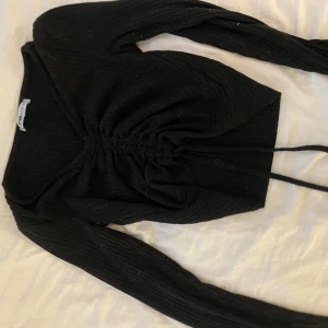 Svart ribbad croppad topp med snörning - Snygg svart långärmad topp från Bik Bok med ribbad struktur och croppad passform. Toppen har en cool snörningsdetalj framtill som gör att du kan justera rynkningen. Perfekt till jeans eller kjol för en trendig look.