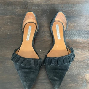 Svarta ballerinaskor från & Other Stories - Snygga svarta ballerinaskor från & Other Stories med spetsig tå och platt sula. Skorna har en cool volangdetalj framtill och är gjorda i mocka med innersula i skinn. Perfekta för dig som gillar stilrena och trendiga skor med en twist.