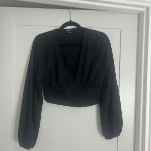 Svart och vit omlottopp från Monki - Två croppade omlottoppar från Monki i svart och vitt. Båda har lång ärm, djup v-ringning och bred resår under bysten. Materialet är ribbat och stretchigt, vilket ger en snygg passform. Perfekta att styla med höga jeans eller kjol.