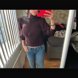 Vinröd stickad polotröja med puffärm - Vinröd stickad polotröja med ribbad struktur och trendiga puffärmar. Tröjan har en tight passform och hög hals, perfekt för dig som gillar en stilren men ändå cool look. Passar perfekt till hösten då man känna sig varm men stilig! 