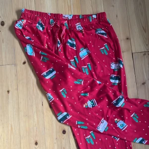 Röda julmönstrade pyjamasbyxor Jonsyn - Röda mjukisbyxor/pyjamasbyxor från Jonsyn med elastisk midja och juligt print av granar och bilar med paket. Byxorna har mudd vid benslut och är perfekta för myskvällar. Materialet är mjukt och stretchigt, vilket gör dem riktigt sköna att ha på sig. Aldrig använda, från USA🤩