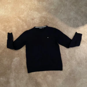 Mörkblå stickad tröja J.Lindeberg - Snygg mörkblå stickad tröja från J.Lindeberg med diskret vitt logobroderi på bröstet. Klassisk rund hals och långa ärmar. Tröjan är stickad i 100% marinull. Passar i åldrarna 10-13 150-165 cm. Perfekt för dig som vill ha en stilren fin tröja till vardagen. Passar till alla årstider. Tröjan ligger nypris runt 1200.                       Först till kvarn, pris kan diskuteras, tveka inte vid minsta lilla fråga 🤗🤝