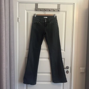Svarta bootcut jeans från Gina Tricot - Knappt använda bootcut jeans från Gina Tricot i svart tvättad denim. Modellen har låg midja, dubbla knappar fram och fickor med lock och knapp bak. Snyggt klassiskt snitt med bredare ben nertill, perfekt för dig som gillar retrovibbar och vill ha en cool siluett.