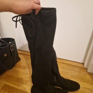 Svarta overknee mockastövlar - Snygga svarta overknee-stövlar i mjuk mocka med platt sula och rund tå. Stövlarna har knytning upptill för att sitta perfekt på benet. Perfekta för att lyfta vilken outfit som helst under kyligare dagar. Använd 1-2 gånger annars nyskick. Nypris: 559kr