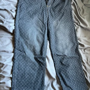 Mönstrade blå jeans med rak passform - Säljer ett par blå jeans med diskret mönster och raka ben. Jeansen har klassiska bakfickor, bälteshällor och kontrastsömmar. Materialet är jeans och de har en snygg tvättad look som sticker ut.