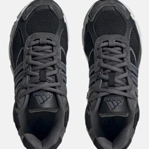 Adidas svarta och grå sneakers - Snygga Adidas sneakers i svart och mörkgrått med klassiska tre ränder på sidan. Ovandelen är i mesh och mocka för en sportig vibe, och sulan är vit med svarta detaljer. Perfekta för dig som gillar streetstyle och bekväma skor med cool design.