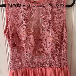 Rosa balklänning - Rosa balklänning i medium med spets upptill och öppen rygg. Köpt på Nelly för några år sedan men endast testad och har tagit av prislappen. Köpt för cirka 1200 om jag inte minns fel
