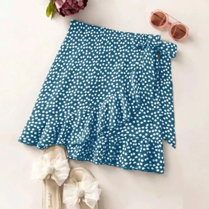 Blommig blå omlottkjol med volang - Supersöt kort omlottkjol i blått med vita blommor och volangkant. Kjolen har knyt i midjan och är gjord i ett lätt och mjukt material som känns skönt mot huden. Storlek S. Köptes för 89kr.