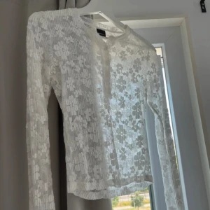 Vit spetsblus från Gina Tricot XS - Supersöt vit blus från Gina Tricot i storlek XS. Blusen är helt i spets med blommigt mönster, har lång ärm och knappar framtill vid halsen. Sitter tight och har en feminin vibe, perfekt till jeans eller kjol. Spetsen är mjuk och stretchig för skön passform.
