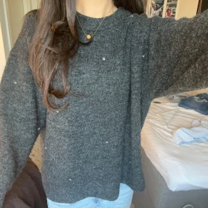 Mörkgrå stickad tröja med diamanter H&M - Mysig mörkgrå stickad tröja från H&M med diamantdetaljer som ger lite extra bling. Tröjan har en loose passform, rund hals och långa ärmar. Perfekt för dig som vill ha något basic men ändå sticka ut något! 🩶🖤