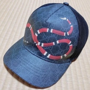 Gucci keps snake svart - Snygg keps från Gucci med klassiskt GG-monogram i grått och svart, prydd med en röd och vit orm på framsidan. Baksidan har mesh och justerbart band med röd och marinblå rand. Perfekt statement-piece för dig som gillar lyxiga accessoarer.