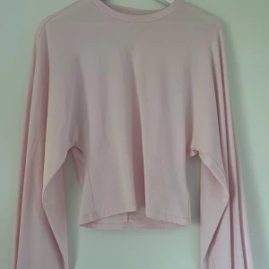 Ljusrosa croppad långärmad tröja - Säljer en ljusrosa långärmad tröja med croppad passform. Tröjan har en enkel och clean design med rund halsringning och är tillverkad i mjuk bomull. 