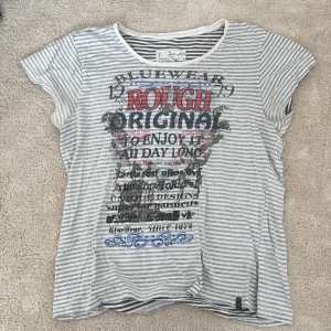 Randig t-shirt från Blue Wear XXL - Snygg t-shirt från Blue Wear i storlek XXL med grå och vita ränder. Tryck framtill i svart, rött och blått med text och grafiska detaljer. Rund halsringning med vit kant och korta ärmar. Den har lite deo stains men det syns knappt. 