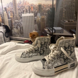 D high-top sneakers monogram 36 - Snygga high-top sneakers från D i vitt och grått med ikoniskt monogrammönster. Skorna har vita snören, rund tå och coola detaljer i silver och svart på sulan. Tillverkade i syntetmaterial och skinn, perfekta för dig som vill sticka ut med lyxig streetstyle.