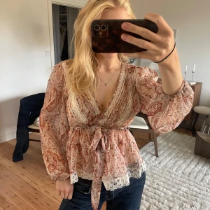 Mönstrad blus  - Säljer en så fin mönstrad blus i fint skick😍Blusen har omlott-design, v-ringning, en dragkedja på sidan, spetsdetaljer vid hals och nederkant samt ett knytband strax under bysten! 