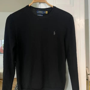 Ralph Lauren Tröja - Jag säljer nu en ruskigt snygg svart stickad Ralph Lauren tröja i storlek S. Den är gjord av merinoull vilket är riktigt skönt material och den är näst intill i nyskick. Tröjan sitter slim och passar till allt. Perfekt till hösten!🙌🍁