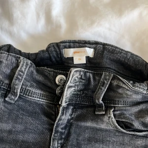 Svarta jeansbyxor från Gina Tricot - Snygga svarta jeansbyxor från Gina Tricot i tvättad look. Byxorna har hög midja, raka ben och coola fickdetaljer med lock och knapp bak. Perfekta för dig som gillar en avslappnad men trendig stil.