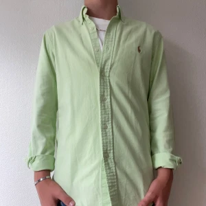 Ljusgrön skjorta från Polo Ralph Lauren - Fräsch ljusgrön skjorta från Polo Ralph Lauren i slim fit-modell. Skjortan har klassisk krage, knäppning framtill och broderad logga på bröstet. Tillverkad i bomull med stretch för extra komfort. Perfekt för dig som gillar stilren och clean look.