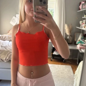 Ribbad röd croppad linnetopp - Säljer en ribbad röd croppad linnetopp med smala axelband och vågig kant nertill. Toppen har en tight passform och är perfekt för varma dagar. Enkel och snygg att matcha med jeans eller kjol.