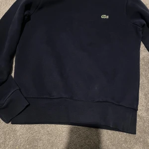 Mörkblå sweatshirt från Lacoste XS - En mörkblå sweatshirt från lacoste som är XS. En skön tröja som är i bra skick och knappast använd. materialet är så bra och känns nice när man har på sig den. Skulle rekommendera att köpa denna tröja, pris kan diskuteras.