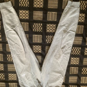 Grå mjukisbyxor från Nike - Snygga ljusgrå mjukisbyxor från Nike med elastisk midja och dragsko. Byxorna har ribbade muddar vid bensluten och en liten vit Nike-logga på låret. Perfekta för chill eller träning, riktigt sköna och stilrena.