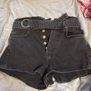 Svarta jeansshorts med bälte H&M Divided - Svarta jeansshorts från H&M Divided med hög midja och snyggt bälte med metallring. Klassisk femficksmodell, framknäppning med silverfärgade knappar och rå kant nedtill. Perfekt till sommarens alla outfits.