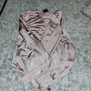 Champagnefärgad omlottopp Gina Tricot - Säljer en champagnefärgad omlottopp från Gina Tricot i glansigt satinliknande material. Toppen har långa ärmar, v-ringning snygg passform. Perfekt för dig som gillar trendiga och stilrena plagg.