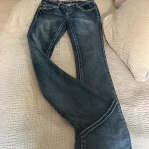 Blå bootcut jeans  - Snygga blå jeans från Amethyst med bootcut passform och coola sömmar. Bakfickorna har coola broderade detaljer och knappar. Jeansen har låg midja och är bootcut!