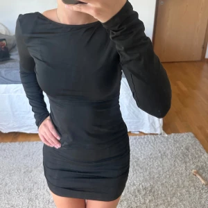 Svart tight miniklänning med öppen rygg - Säljer en svart, figurnära miniklänning med lång ärm och snygg öppen rygg. Klänningen har en enkel, stilren design och är gjord i ett stretchigt material som sitter skönt mot kroppen. Perfekt för dig som gillar minimalistisk stil med en twist.