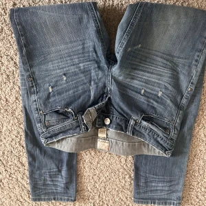 Blå jeans från Ardene med slitningar - Säljer ett par blå jeans från Ardene med snygga slitningar och tvättade detaljer. Jeansen har klassisk femficksdesign och raka ben. Materialet är bomull med lite stretch för skön passform. Perfekta för en avslappnad och trendig look.