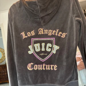 Juicy Couture brun velour hoodie M - Trendig brun kofta från Juicy Couture i velour med dragkedja, huva och snörning. Stor broderad logga och text i guld och rosa på ryggen⭐️. Inga defekter, använd en gång!🫶🏼säljer pga att den inte kommer till användning 