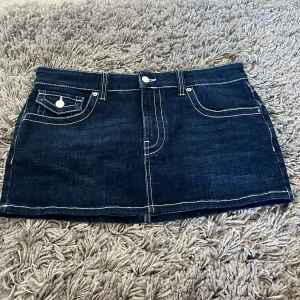 Mörkblå jeanskjol från Topshop - Säljer en snygg mörkblå jeanskjol från Topshop med kontrastsömmar och coola fickdetaljer både fram och bak. Kjolen har bälteshällor och knäppning framtill. Perfekt för dig som gillar en klassisk men trendig look.