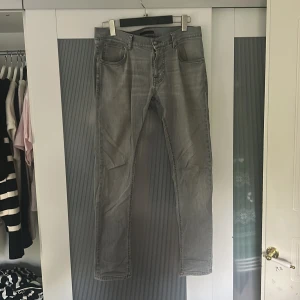 Grå jeans från Nudie Jeans Co - Snygga grå jeans från Nudie Jeans Co med klassisk femficksdesign och diskreta sömmar på bakfickorna. Jeansen har en smal passform och är tillverkade i mjukt denimtyg. Perfekta för dig som gillar en stilren och enkel look. 34 32