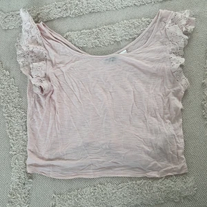Ljusrosa topp med spetsärmar från H&M - Supersöt ljusrosa topp från H&M Divided i storlek S. Toppen har korta ärmar med volangig spetsdetalj och en lös, luftig passform.