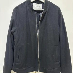 Svart vår/höstjacka från These Glory Days - Stilren svart bomberjacka från These Glory Days med klassisk ribbad krage och hel dragkedja framtill. Jackan är tillverkad i ett mjukt material som känns skönt att bära. Tveka inte på att ställa frågor. Ny pris runt 1250 kronor. Priset kan diskuteras 