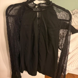 Svart spetsblus från Vila Rouge - Supersnygg svart blus från Vila Rouge med transparenta spetsärmar och hög hals. Blusen har knäppning i nacken.Super fin spets tröja! Den är smal om armarna men passar en som normalt viss har xs-s 💖