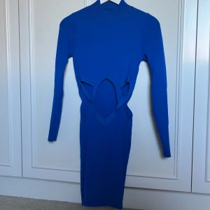 Blå långärmad cut out klänning Zara - Säljer en blå långärmad klänning från Zara med coola cut out-detaljer i midjan. Klänningen är kroppsnära och har en hög hals. Materialet är ribbat och stretchigt, vilket ger en snygg passform. Perfekt för dig som vill sticka ut med en trendig look.