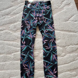 Mönstrade träningstights från Stronger XS - Säljer ett par färgglada träningstights från Stronger i storlek XS. De har ett tropiskt mönster i grönt, lila och blått på svart botten och är högmidjade. Perfekta för träning eller chill dagar. Materialet är stretchigt och bekvämt.