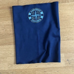 Blå Djurgården halsduk i polyester - Snygg marinblå halsduk/buff med Djurgården Stockholm-logga framtill. Perfekt för att visa ditt stöd på matchen eller när du är ute och rör på dig. Tillverkad i mjuk polyester som är skön mot huden och lätt att bära.