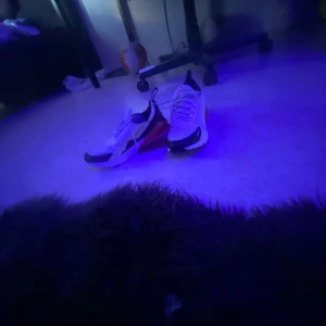 Nike Air Max 270 vita och röda sneakers - Nike Air Max 270 sneakers i vitt med svarta och röda detaljer. Snygg design med stor synlig Air-enhet i hälen och mesh-ovandel för bra andningsförmåga. Perfekta för dig som vill ha en sportig och modern look. Klassisk Nike-logga på sidan och snörning framtill.