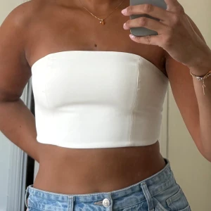 Vit bandeautopp med snörning - Säljer en stilren vit bandeau tubtopp från NA-KD x Hanna Schönberg. Toppen är axelbandslös och har snygg snörning i ryggen som ger en cool och justerbar passform. 