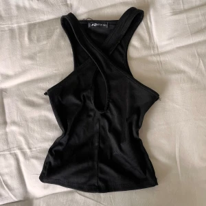 Croppad halterneck - Svart ribbad, croppad, halterneck ifrån från Newyorker (fb sisters). Toppen har en snygg omlott-design framtill med cut-out detalj vid bröstet och breda axelband. 