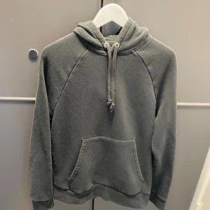  hoodie från A Day's March - Mysig mörkgrå hoodie från A Day's March med huva och dragsko. Tröjan har en stor magficka och ribbade muddar vid ärmslut och nederkant. Perfekt för en avslappnad stil. (Nypris 1200)
