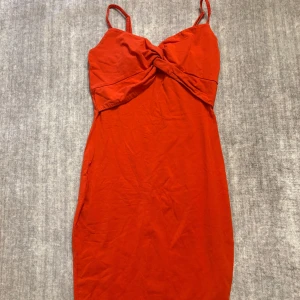 Röd klänning med twistdetalj från Amisu - Säljer en röd klänning från New Yorker med smala axelband och snygg twistdetalj framtill. Klänningen har en figurnära passform och är perfekt för dig som gillar en enkel men stilren look.