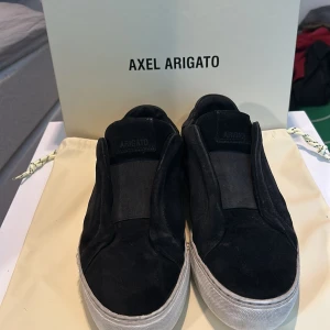 Svarta slip-on sneakers Axel Arigato - Svarta mocka skor från Axel Arigato, skorna har slitningar på sulan men förövrigt så är skorna i fint skick. Box och dustbag ingår.