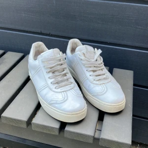 Vita Valentino Garavani sneakers 38,5 - Snygga vita sneakers från Valentino Garavani i skinn med coola nitar baktill på sulan. Klassisk rund tå, snörning och diskret logga på plösen. Perfekta för dig som gillar stilrena men ändå unika skor.