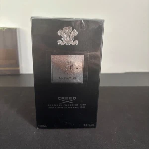 Aventus Eau de Parfum 100ml från Creed - Lyxig parfym från Creed, Aventus Eau de Parfum i svart förpackning med silverdetaljer. Flaskan rymmer 100 ml och är känd för sin eleganta och maskulina doftprofil. Perfekt för dig som vill sticka ut med en exklusiv signaturdoft.